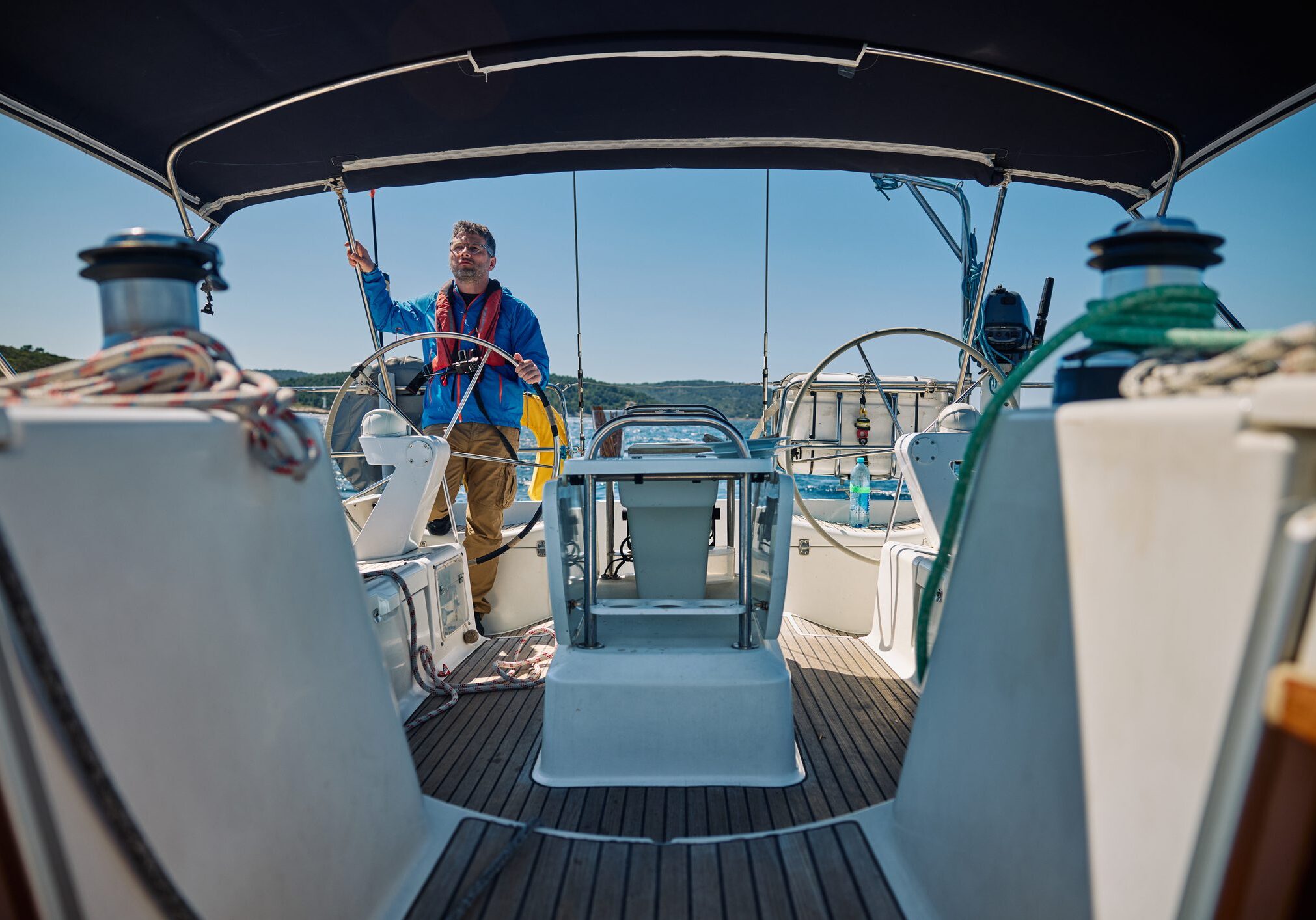 Person steering sailboat on sunny day.